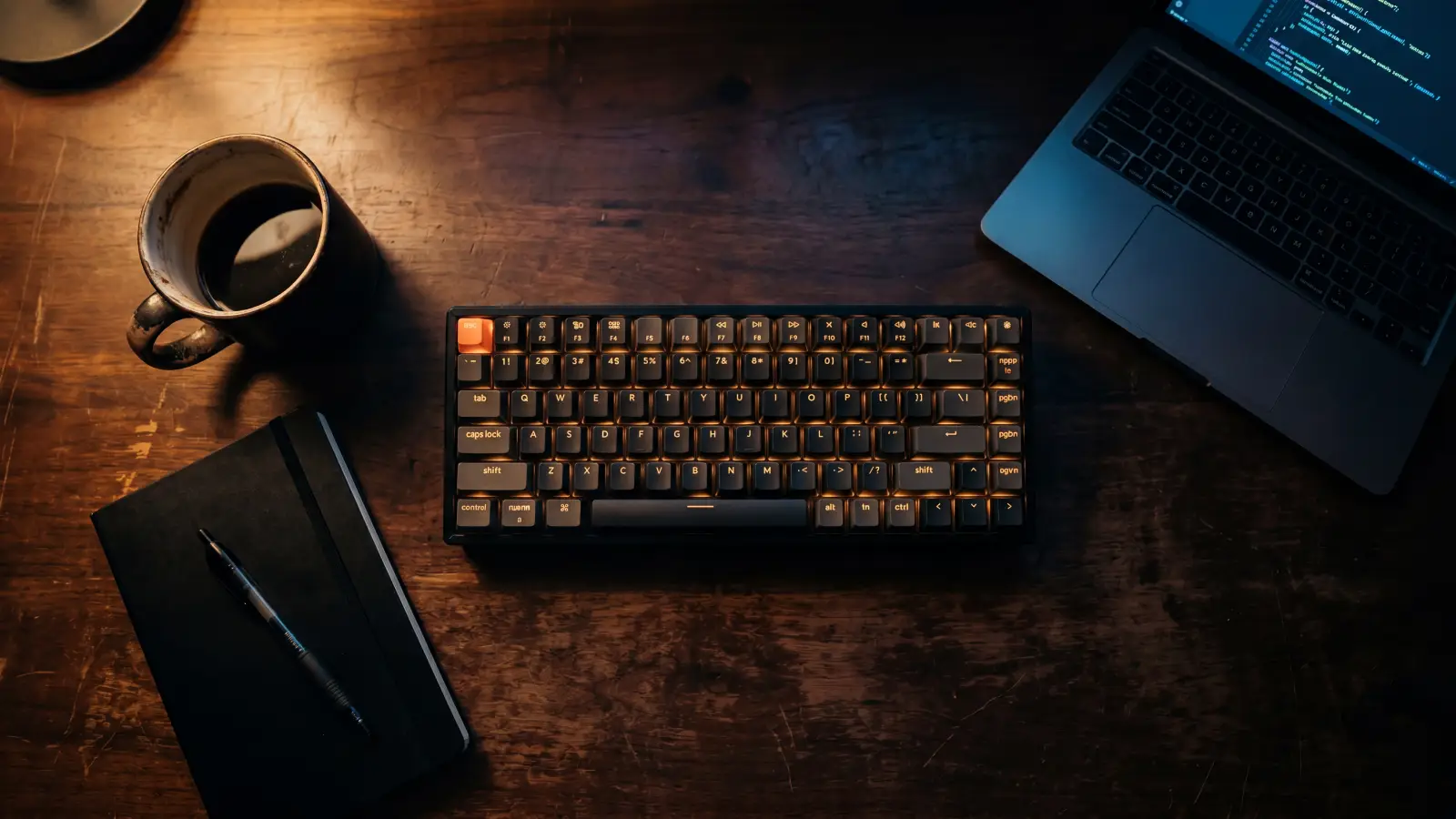 A developer's desk at night, with a backlit keyboard and a coffee cup in warm light